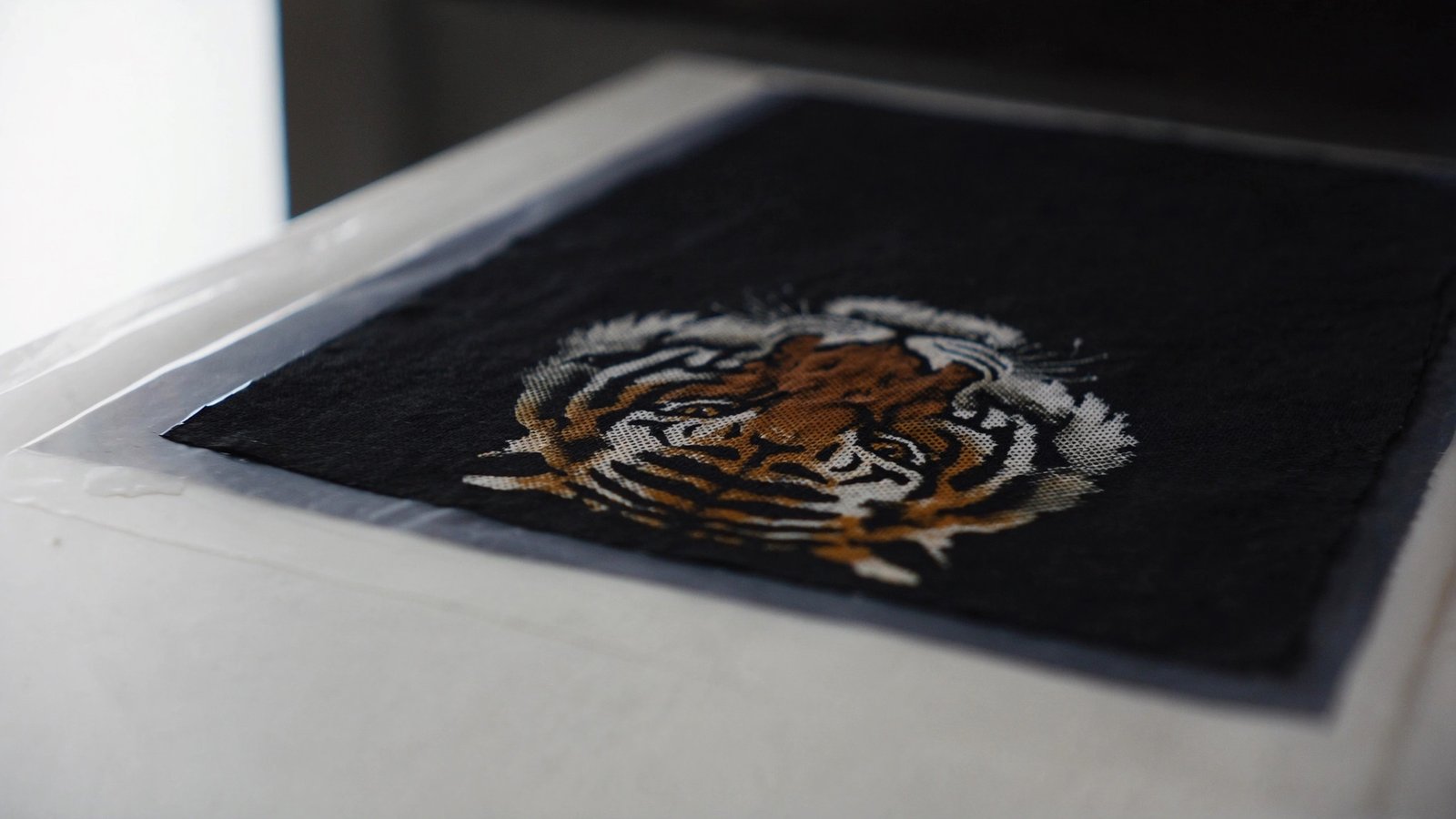 Black fabric on a heat press with a halftoned DTF tiger print where the black areas let the fabric show through between the colour dots